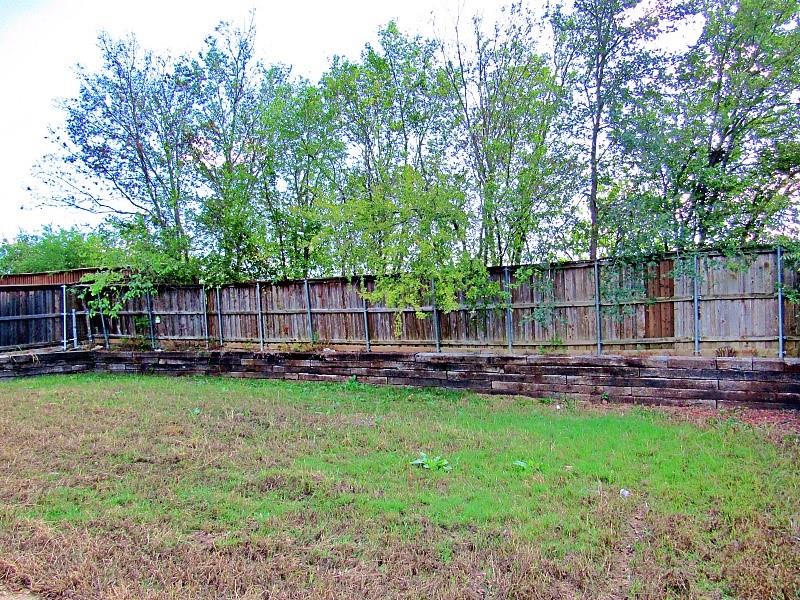 Backyard featuring a tiered timber retaining wall, vertical wood fencing, and mature trees