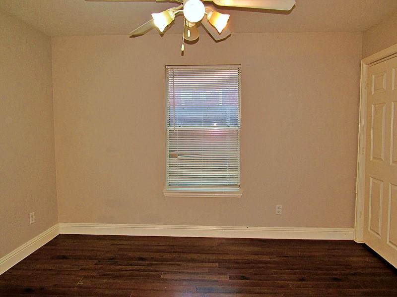 Interior room featuring dark wood-finish flooring, neutral wall paint, a central ceiling fan with multi-directional lighting, a single window with slatted blinds, and a six-panel interior door