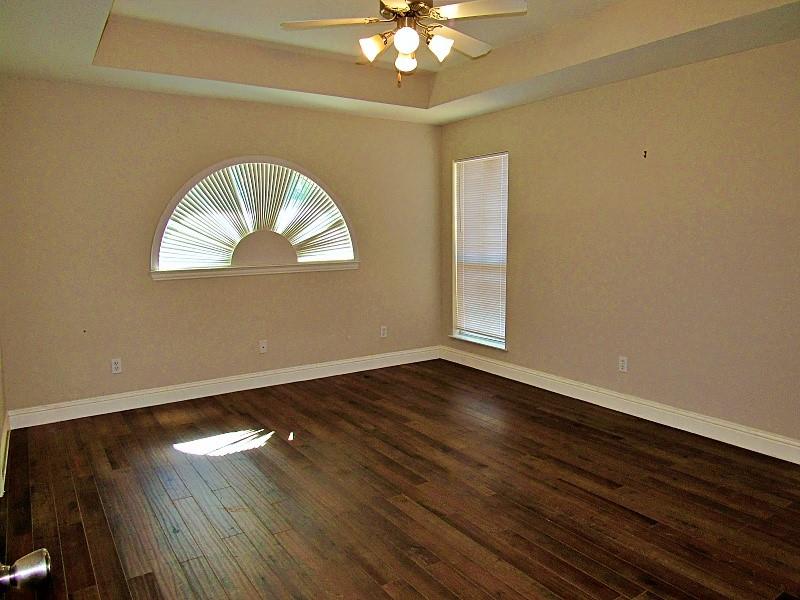 Tray ceiling with a central multi-light fan, wood-finish flooring, and a decorative arched window