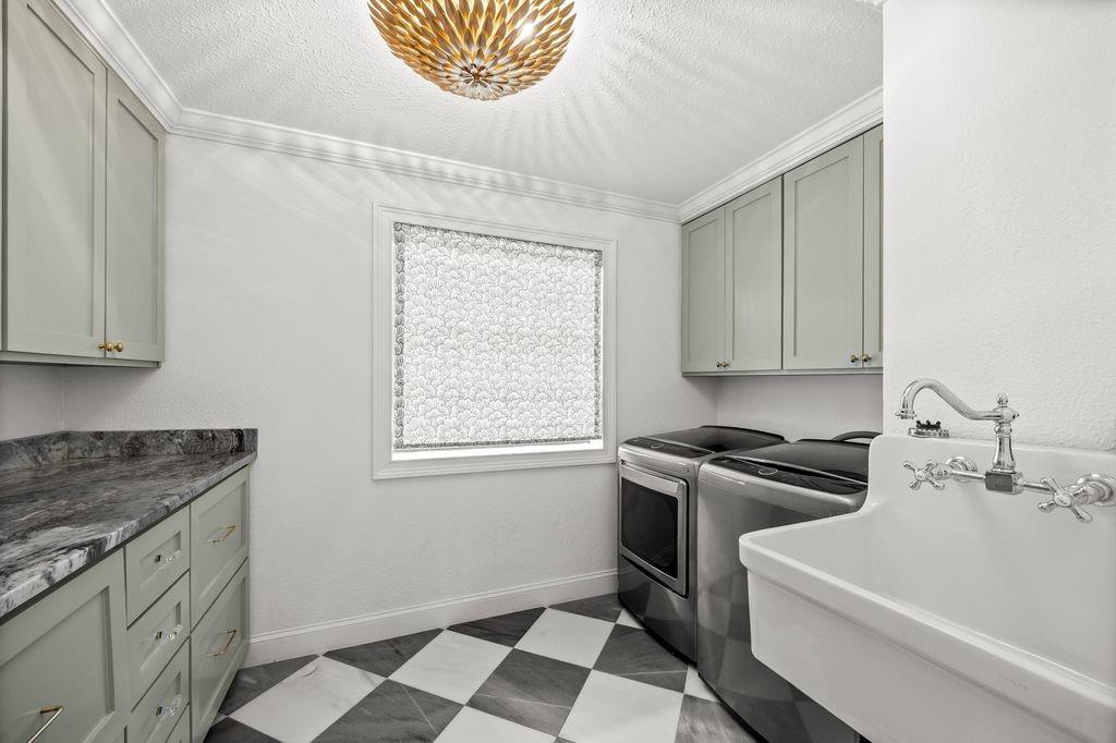Utility room featuring sage-toned cabinetry, stone-patterned countertops, a wall-mounted utility sink with polished chrome hardware, and black and white checkerboard flooring