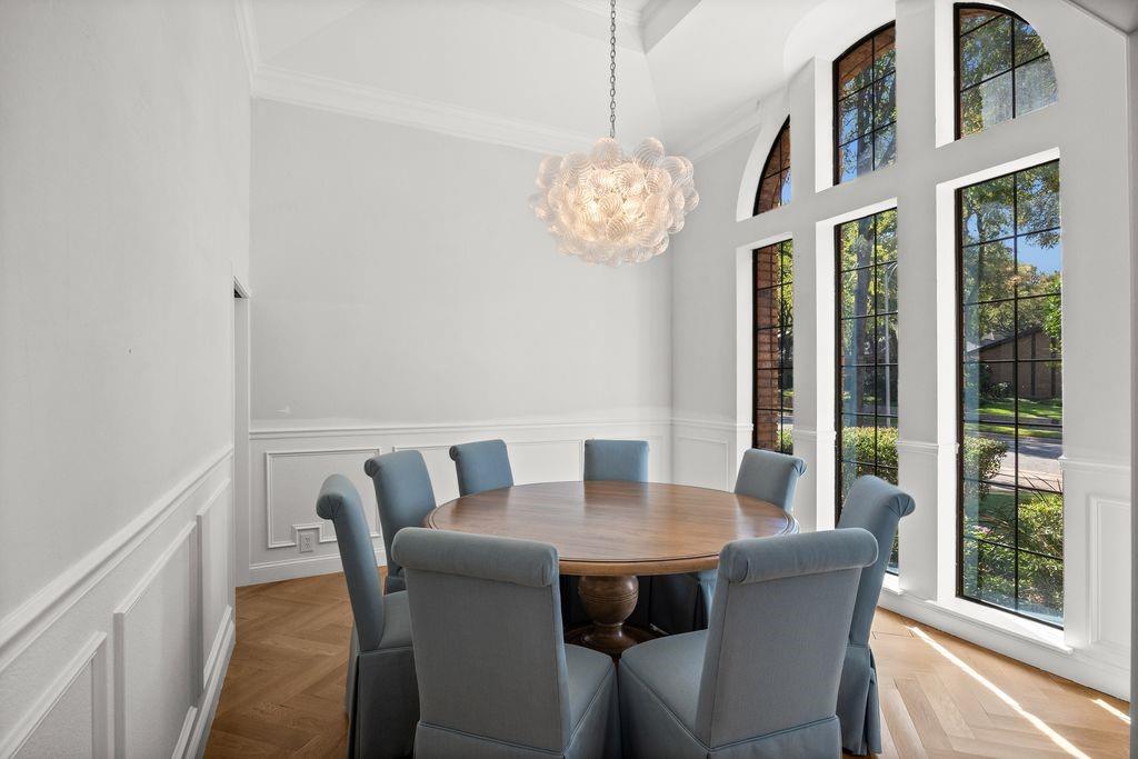 Vaulted ceilings featuring decorative molding, floor-to-ceiling arched windows with grid detailing, herringbone wood-finish flooring, and wainscoting