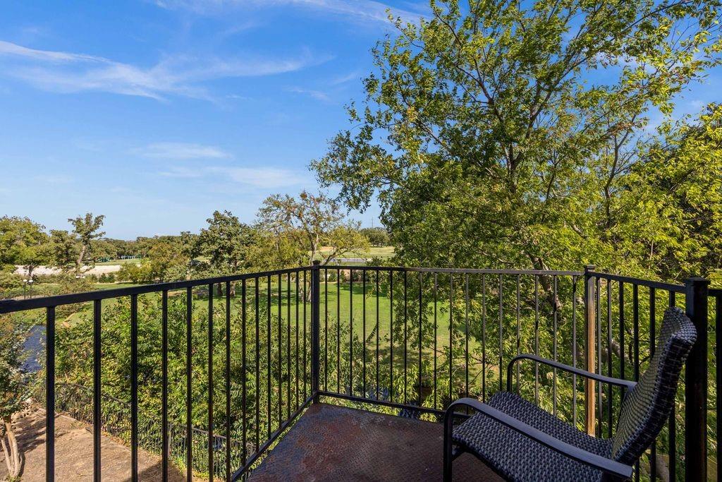 Elevated balcony featuring a metal railing and textured flooring overlooking mature trees and open green space