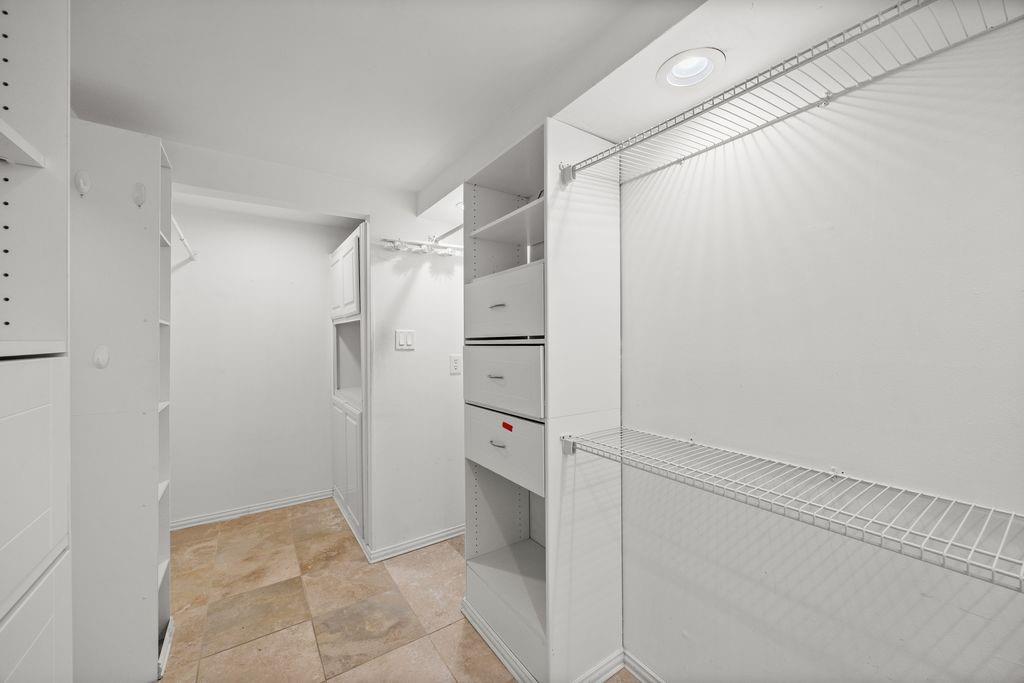 Custom walk-in closet featuring white built-in cabinetry, integrated drawers, wire shelving, and stone-finish flooring with recessed lighting