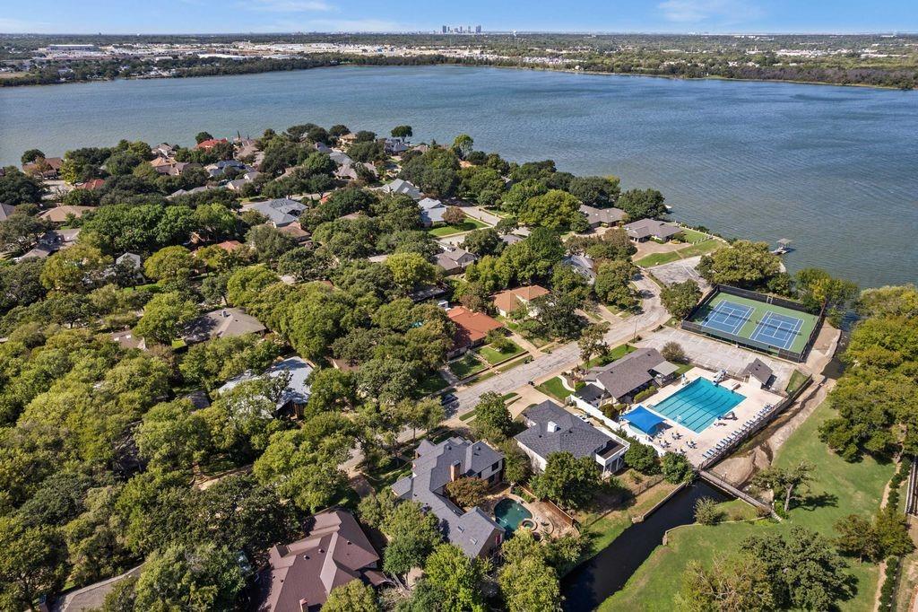 Aerial perspective of a lakeside neighborhood featuring mature trees, a community swimming pool, and tennis courts