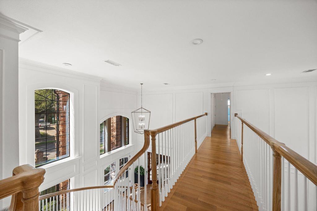 Gallery landing featuring wood-finish flooring, white panel molding, wood-capped railings with vertical balusters, arched multi-pane windows, and a geometric pendant light fixture