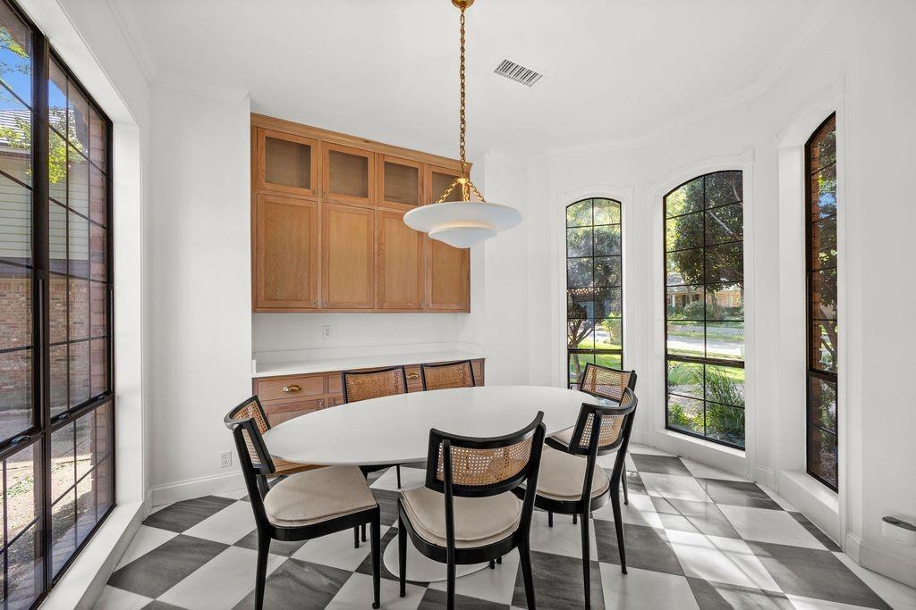 Sun-drenched dining area featuring large arched grid-pattern windows, custom wood-finish built-in cabinetry, and diamond-pattern stone tile flooring accented by a tiered metal pendant light fixture