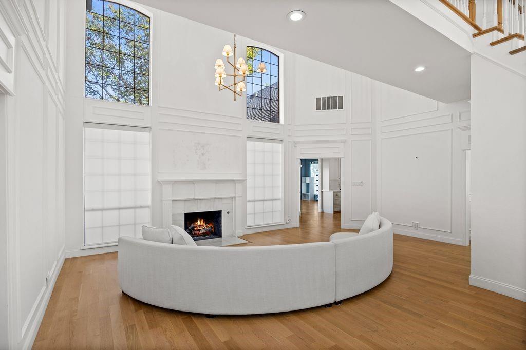Double-height ceiling featuring extensive wall paneling, tall arched windows, wood-finish flooring, and a fireplace with a traditional mantle