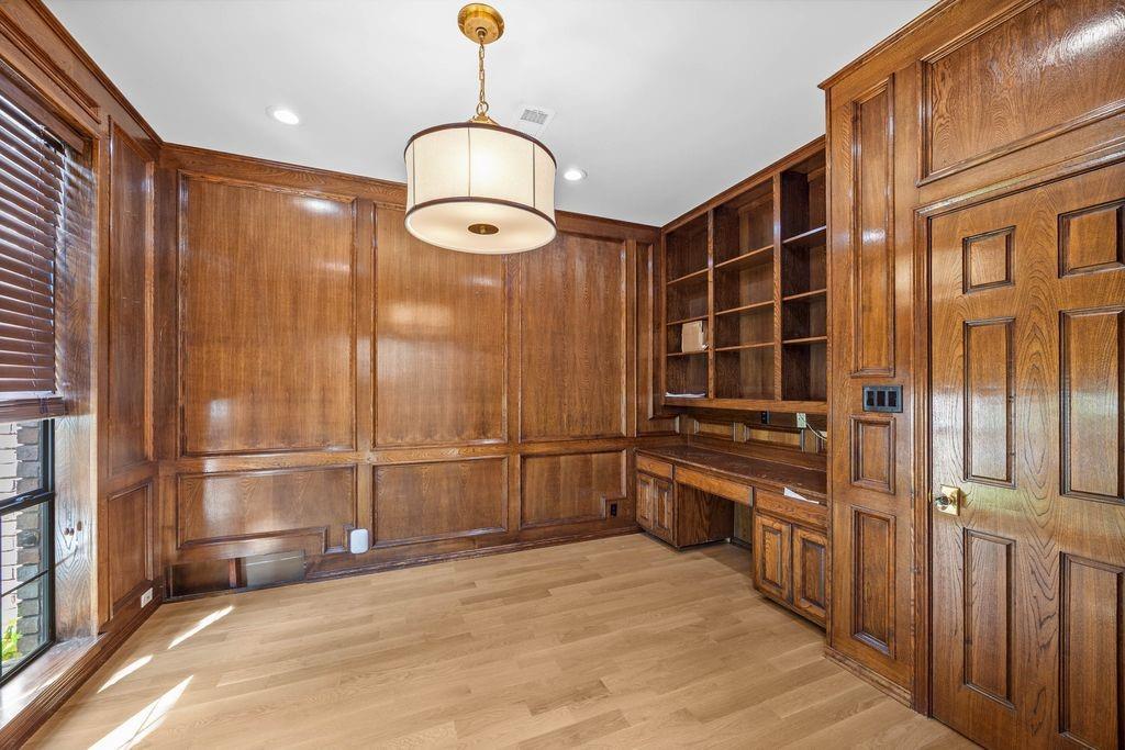 Wood-paneled walls with intricate millwork, built-in floor-to-ceiling cabinetry, integrated desk space, wood-finish flooring, and a drum-style pendant light fixture