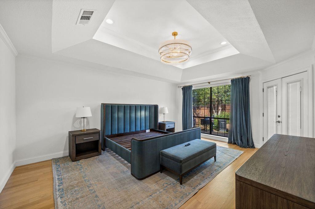 Tray ceiling featuring recessed lighting and a multi-tiered circular chandelier, wood-finish flooring, and a large window with black muntins