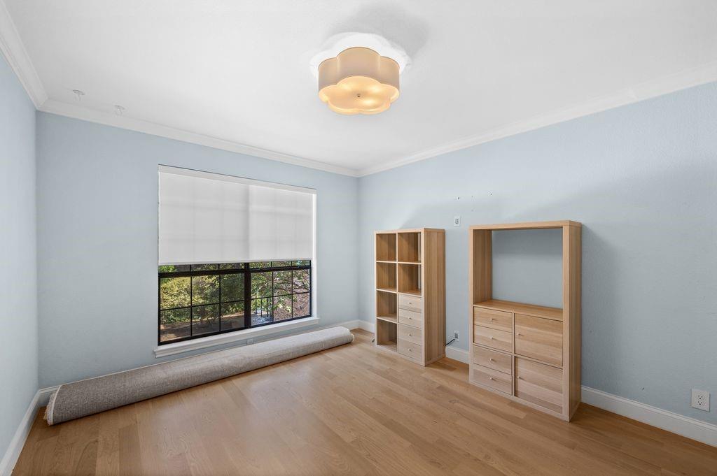 Room featuring wood-finish flooring, crown molding, a large multi-pane window, and a decorative flush-mount ceiling light fixture