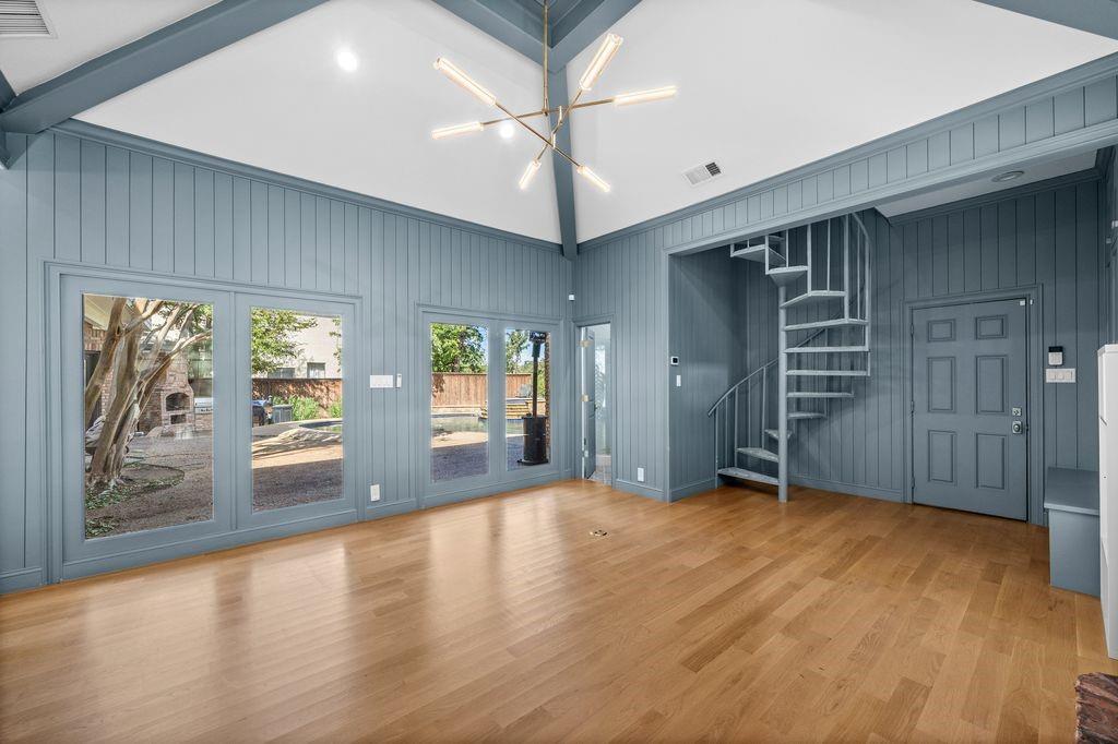 Vaulted ceiling with exposed beams, wood-finish flooring, vertical plank wall paneling, metal spiral staircase, and multi-panel glass doors