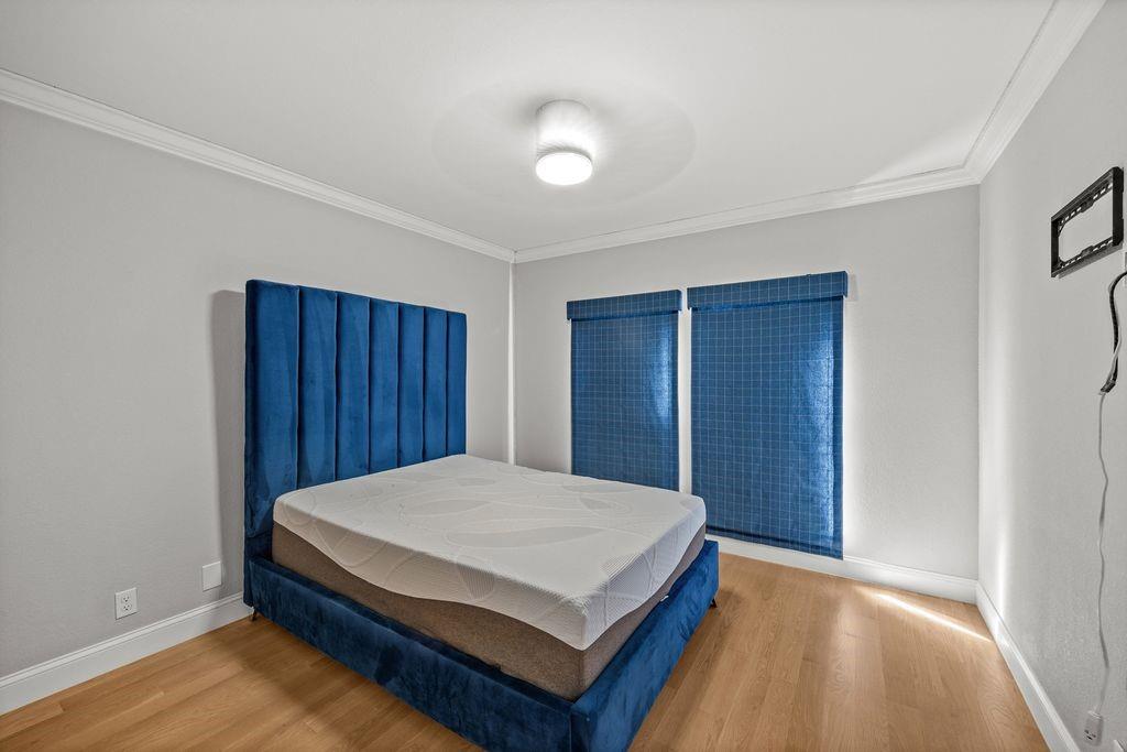 Room featuring wood-finish flooring, crown molding, and two windows with blue grid-patterned roller shades