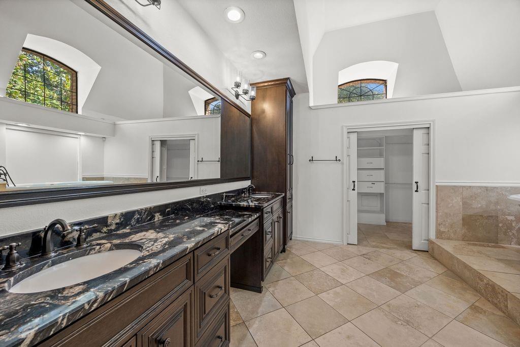 Double vanity featuring dark wood cabinetry, integrated stone countertops with dual undermount sinks, full-width mirror, recessed lighting, and built-in linen storage