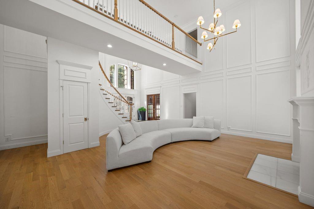 Double-height ceiling, decorative wall paneling, curved staircase with wood railings, wood-finish flooring, and multi-arm chandelier
