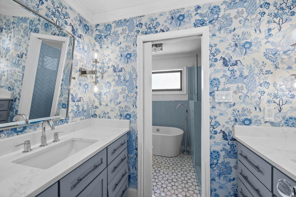 Dual vanities with solid-surface countertops, custom blue cabinetry, chrome wall-mounted lighting, and a freestanding soaking tub with floor-mounted faucet