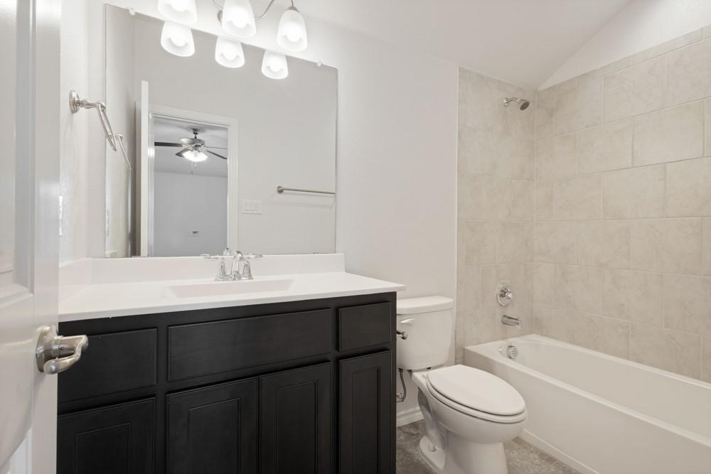 Dark-finish vanity cabinetry with a white countertop and integrated sink, full-width mirror, polished chrome plumbing fixtures, and tile-surround tub