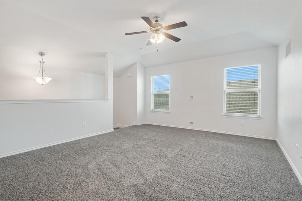 Vaulted ceilings, neutral carpeting, a central ceiling fan with integrated lighting, and dual windows