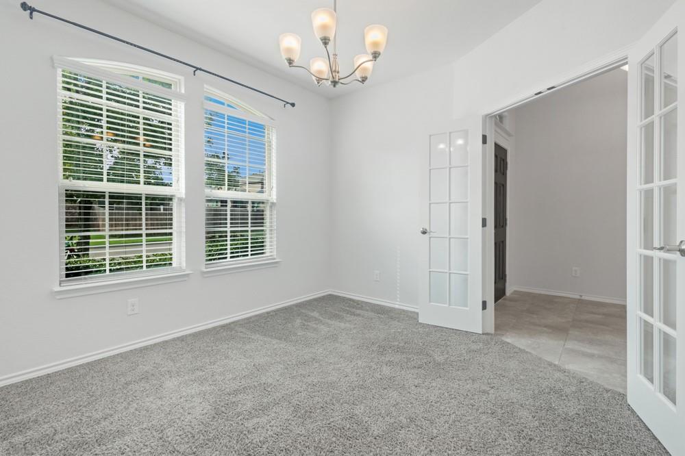 Room featuring carpeted flooring, arched windows, multi-pane French doors, and a five-light chandelier