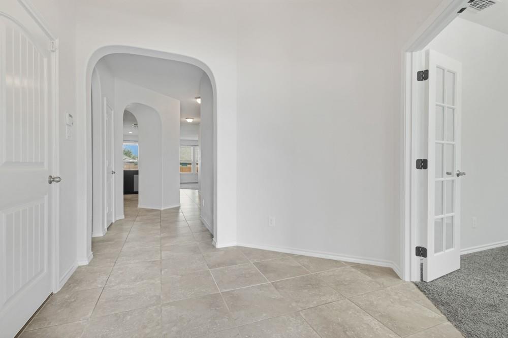 Interior entryway featuring oversized tile flooring, multiple arched doorways, and French doors with glass panes