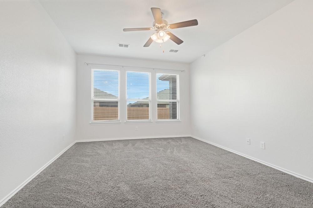 Neutral-toned interior room featuring wall-to-wall carpeting, three windows with horizontal blinds, and a ceiling fan with integrated lighting