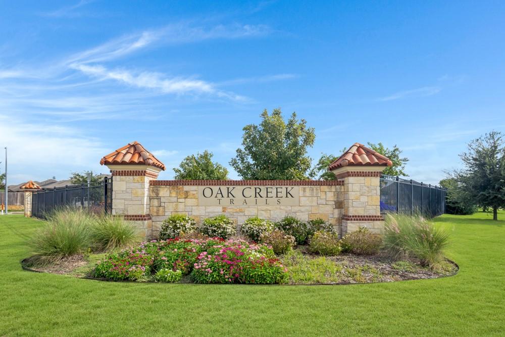 Community entrance featuring a stone-clad monument sign with tile-capped pillars, decorative masonry details, and professional landscape beds