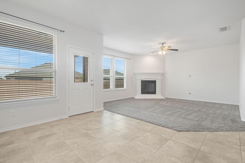 Open-concept interior featuring large-format tile flooring, plush carpeting, a corner fireplace with a mantel, and a ceiling fan