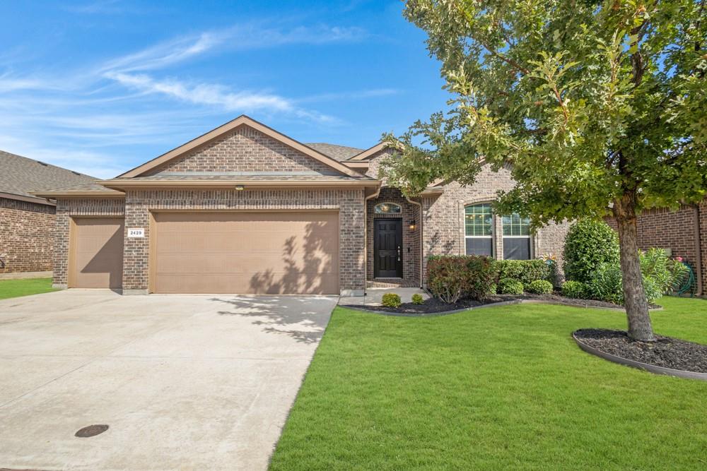 Brick exterior featuring a multi-car garage, arched entryway with a paneled door, decorative gable detail, and manicured front lawn