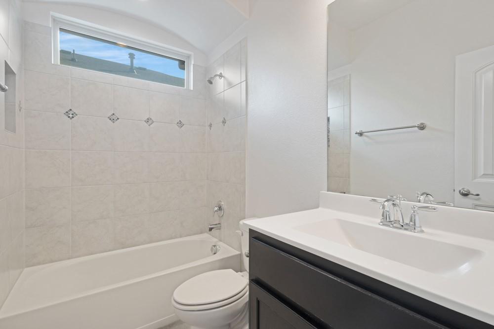 Bathroom featuring a vanity with a white countertop and dark cabinetry, a combination shower and tub with neutral tile surround, a transom window, and a full-width wall mirror