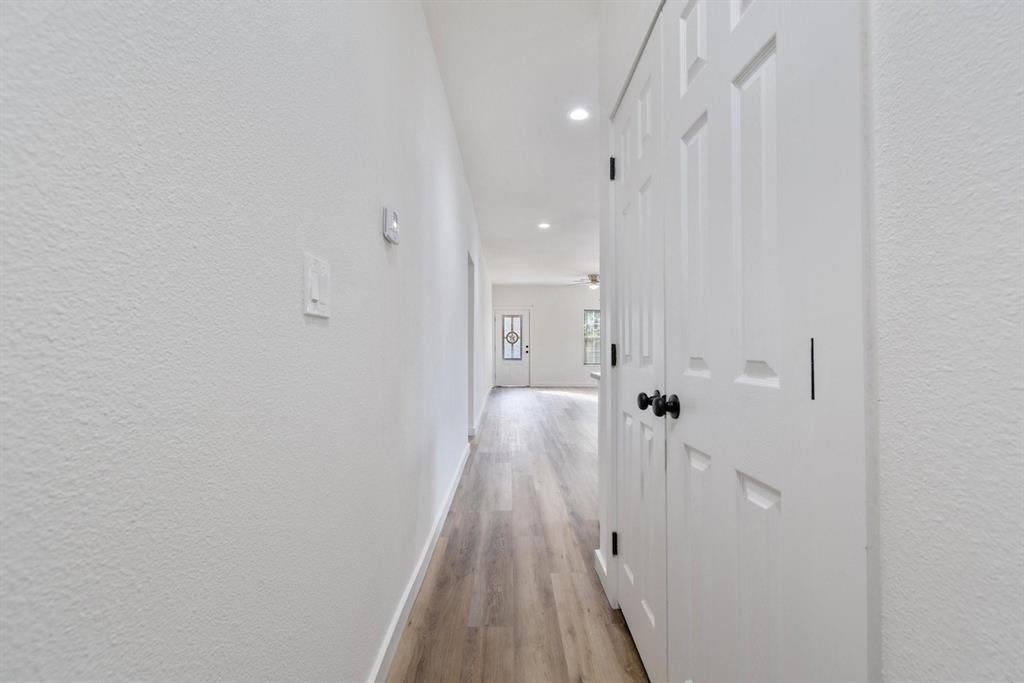 Hallway featuring wood-finish flooring, white textured walls, recessed ceiling lighting, and a six-panel closet door with black hardware