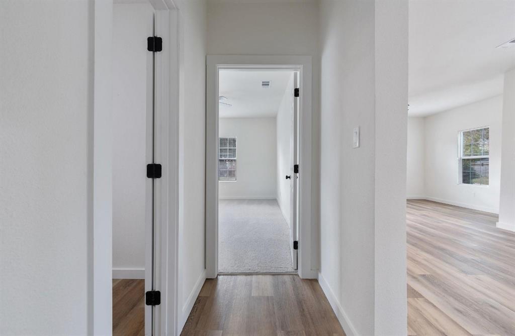 Interior hallway featuring neutral-toned wall paint, wood-finish flooring, and doorways accented with matte black hinges
