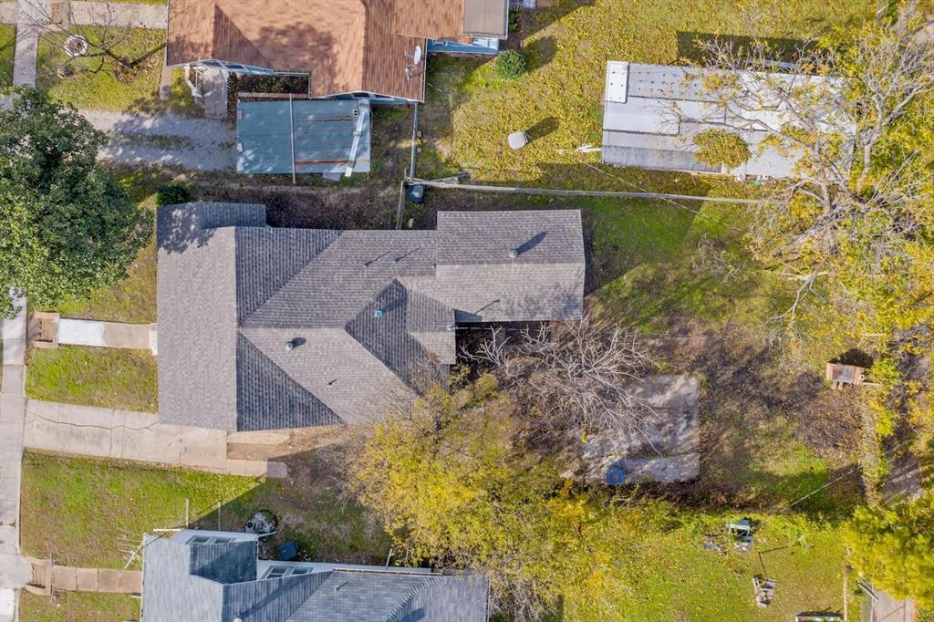 Aerial perspective featuring an asphalt shingle roof, paved driveway, expansive lawn, and mature trees