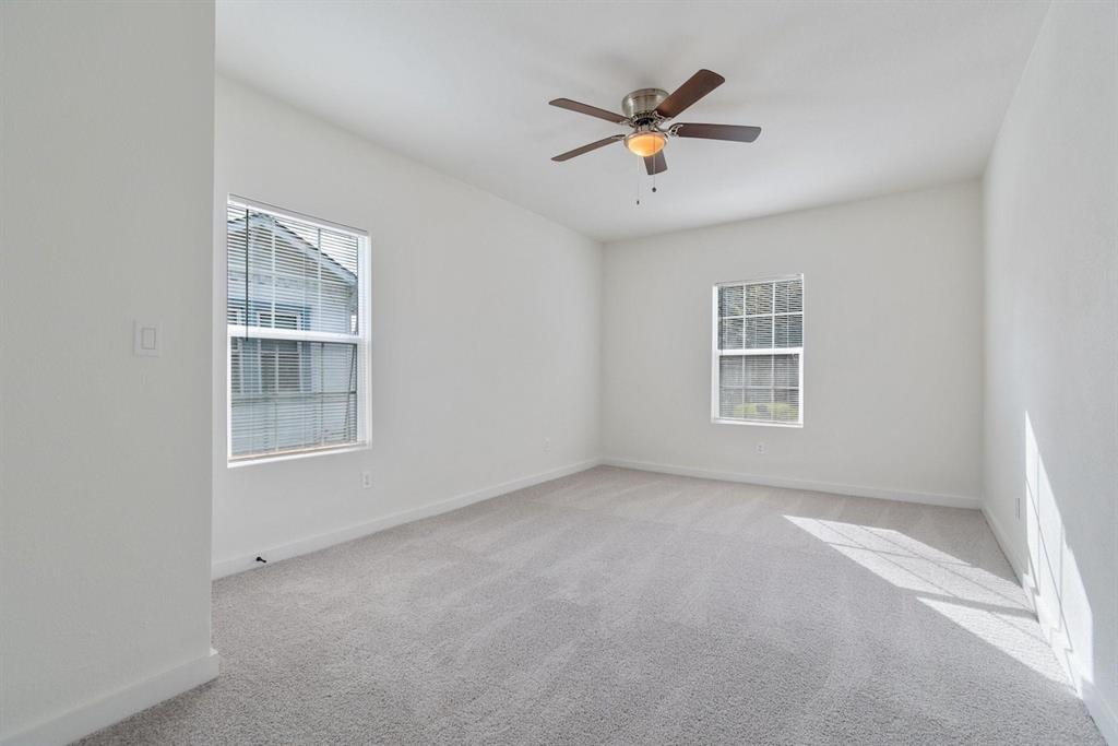 Neutral interior space featuring wall-to-wall carpeting, dual windows, and a central ceiling fan with integrated lighting