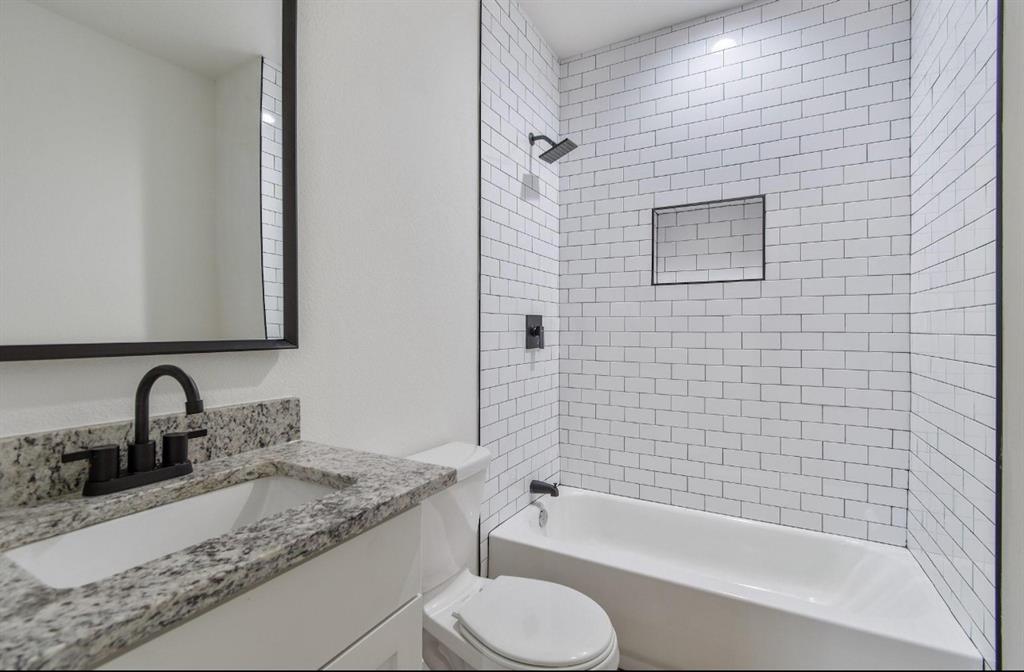 Bathroom featuring a stone-look countertop, undermount sink, matte black faucet and fixtures, and a shower-tub combination with white subway tile surround and a recessed niche