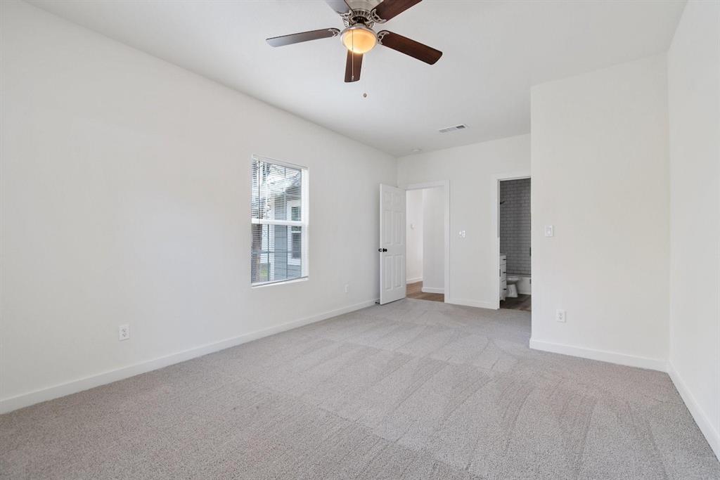 Neutral-toned wall-to-wall carpeting, central ceiling fan with integrated lighting, single-pane window, and interior door leading to a tiled-finish bathroom