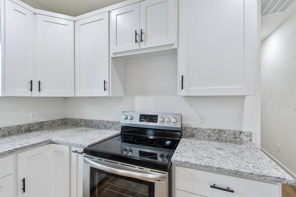 White shaker-style cabinetry with matte black hardware, stone-patterned countertops, and a stainless steel freestanding range