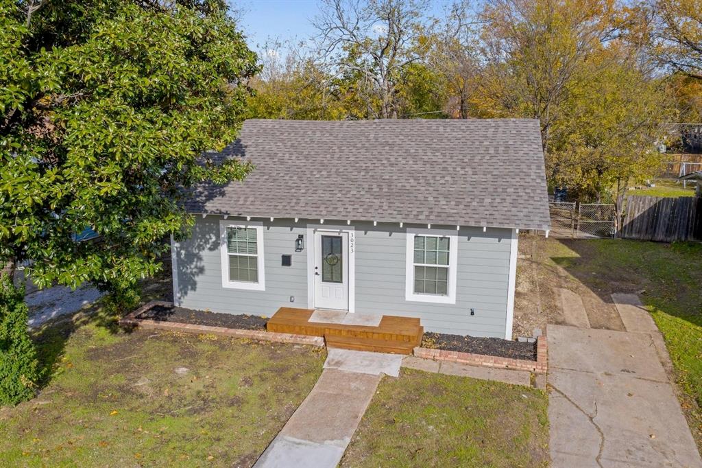 Single-story residence featuring light gray siding, a composite shingle roof, a wood-finished front porch, and brick-edged garden beds