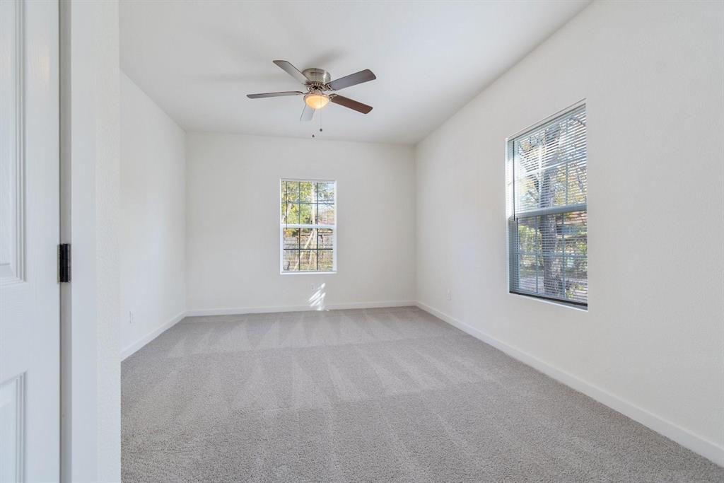 Neutral-toned carpeted interior featuring a ceiling fan with integrated lighting and two windows with horizontal blinds