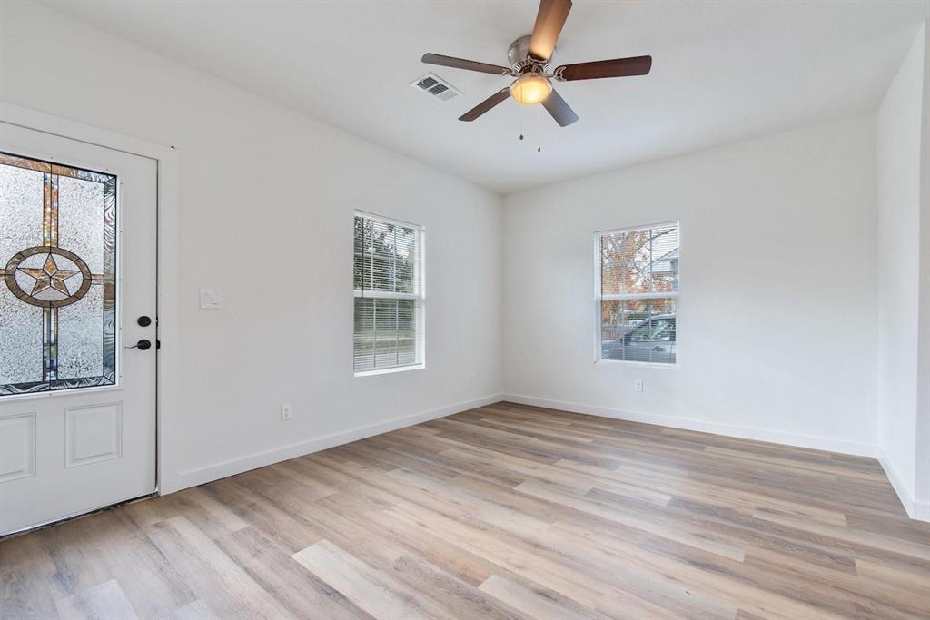 Interior room featuring wood-finish flooring, two dual-pane windows, a ceiling fan with integrated lighting, and an exterior door with a decorative glass insert