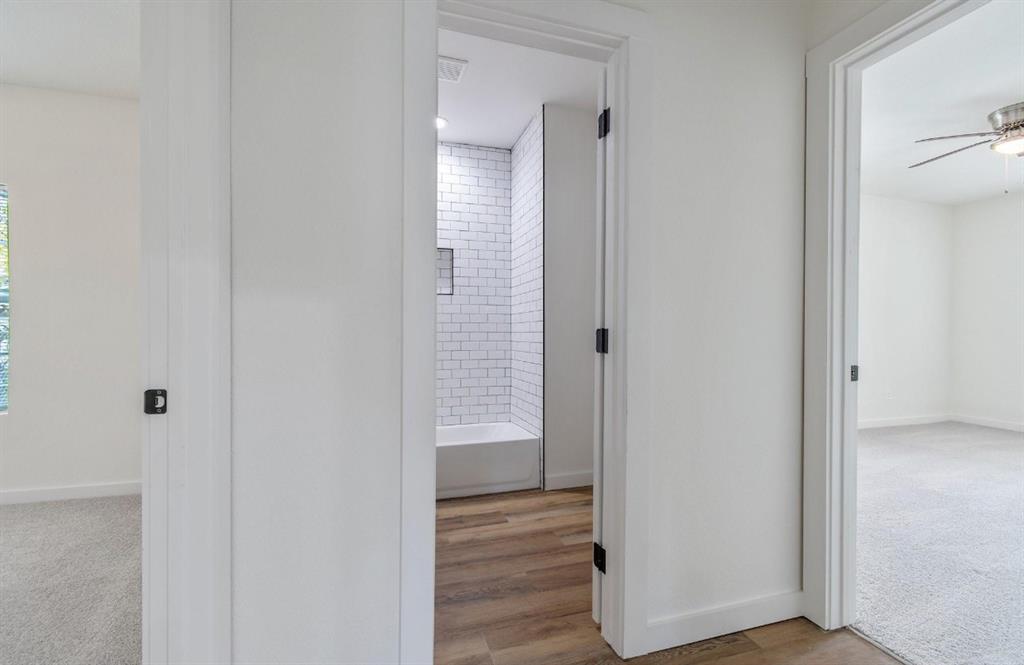 Interior featuring white subway tile shower surround with recessed niche, wood-finish flooring, and black hardware accents on crisp white doors