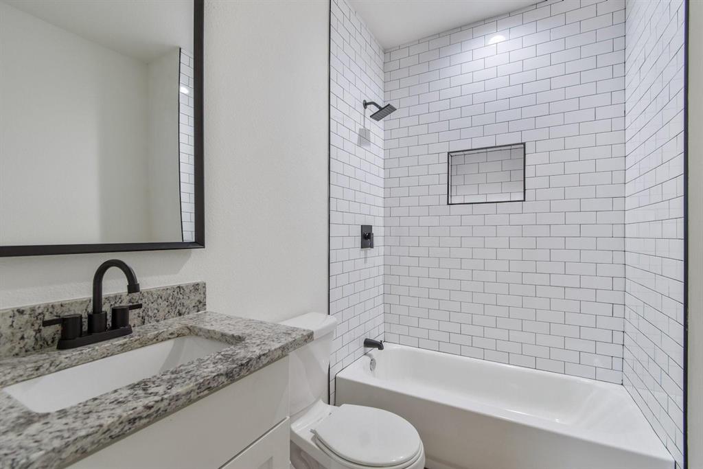 Bathroom featuring a vanity with a stone-finish countertop, white subway tile shower surround with integrated wall niche, matte black fixtures, and a framed mirror