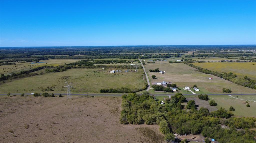 Expansive acreage featuring cleared pasture land, clusters of mature trees, and paved road access