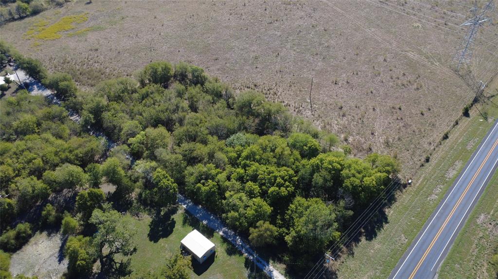 Expansive lot featuring mature hardwood trees, open grassland, and a single-story outbuilding with a metal roof