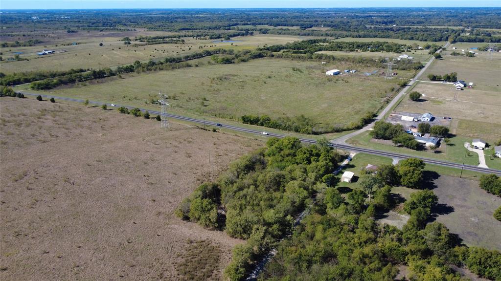 Expansive acreage featuring cleared pastureland, mature tree clusters, and paved road frontage