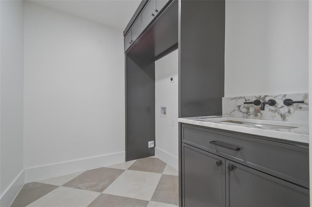 Dark gray built-in cabinetry, stone-finish countertop with integrated sink, matte black wall-mounted faucet, and geometric tile flooring