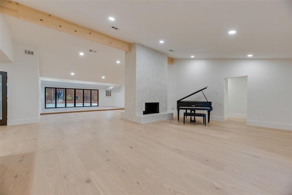 Open-concept living space featuring wood-finish flooring, recessed lighting, exposed wooden ceiling beams, and a centrally located floor-to-ceiling fireplace with a masonry finish