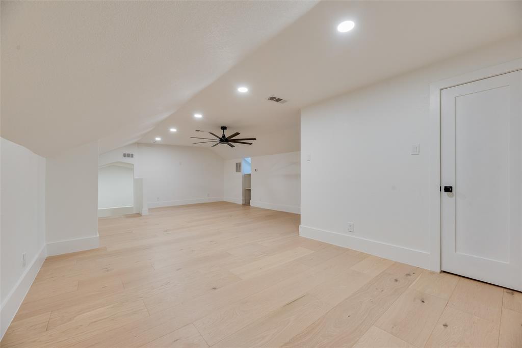 Expansive room featuring sloped ceilings, light-toned wood-finish flooring, recessed lighting, and a matte black ceiling fan
