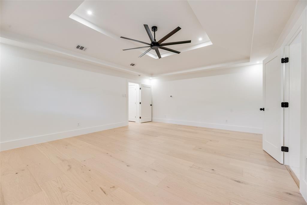 Tray ceiling featuring recessed lighting and a multi-blade ceiling fan, complemented by light-toned wood-finish flooring and solid core interior doors