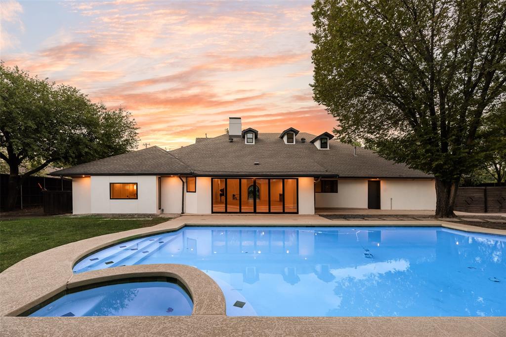 In-ground swimming pool with integrated spa and aggregate stone decking, multi-panel folding glass doors, and dormer windows