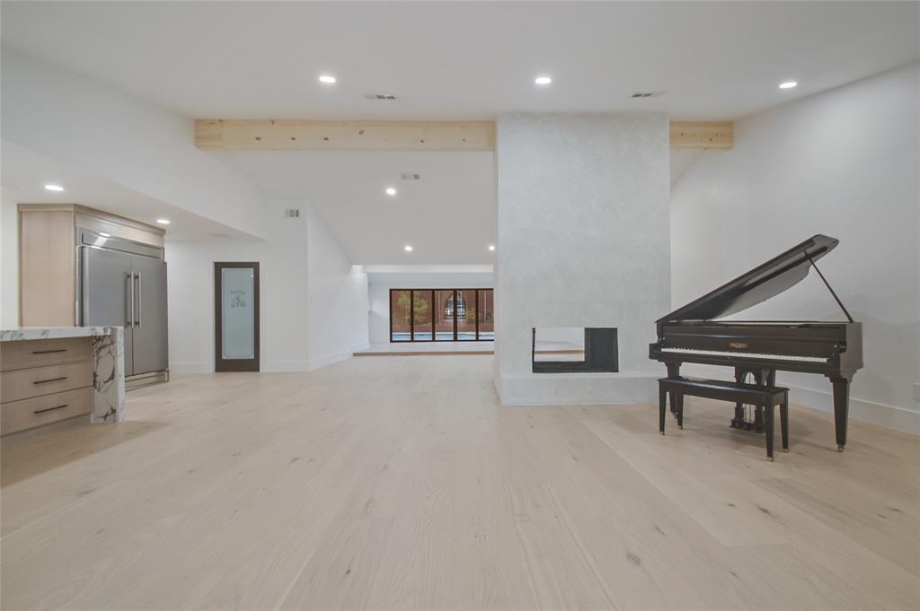 Open-concept living space featuring wood-finish flooring, recessed lighting, exposed structural beams, a central fireplace with a smooth plaster finish, and built-in cabinetry with stone-finish countertops