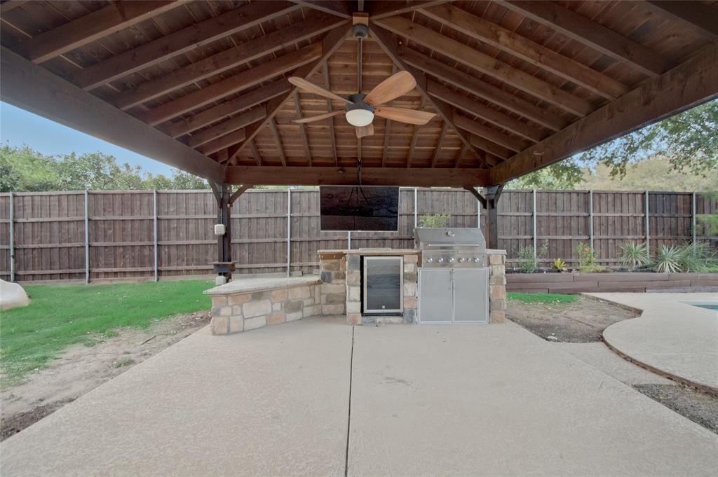 Covered outdoor kitchen pavilion featuring a timber-frame ceiling, integrated stone masonry, built-in stainless steel grill, under-counter refrigeration, and ceiling fan